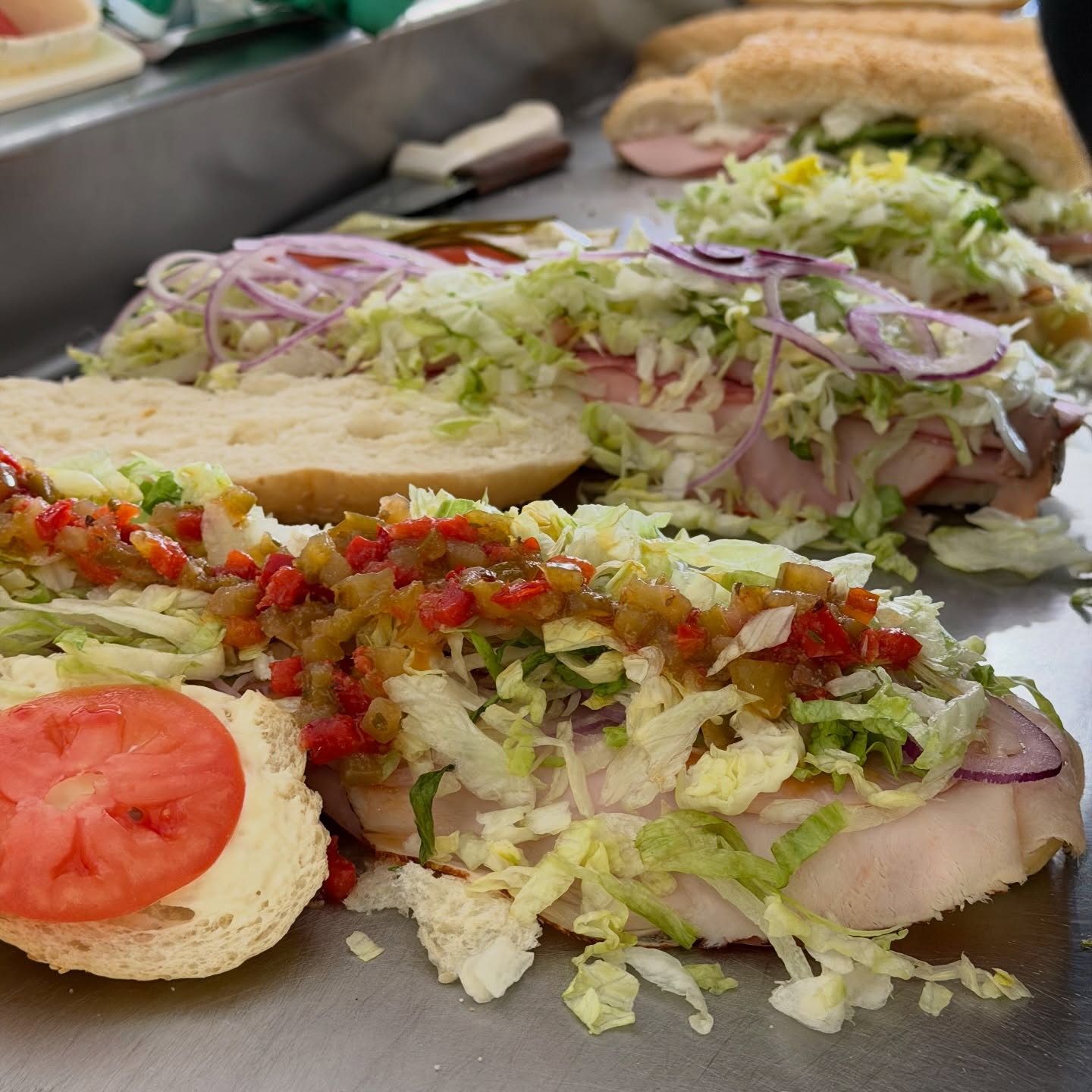 Dino's subs being dressed with lettuce, onions, tomatoes and relish on the prep counter