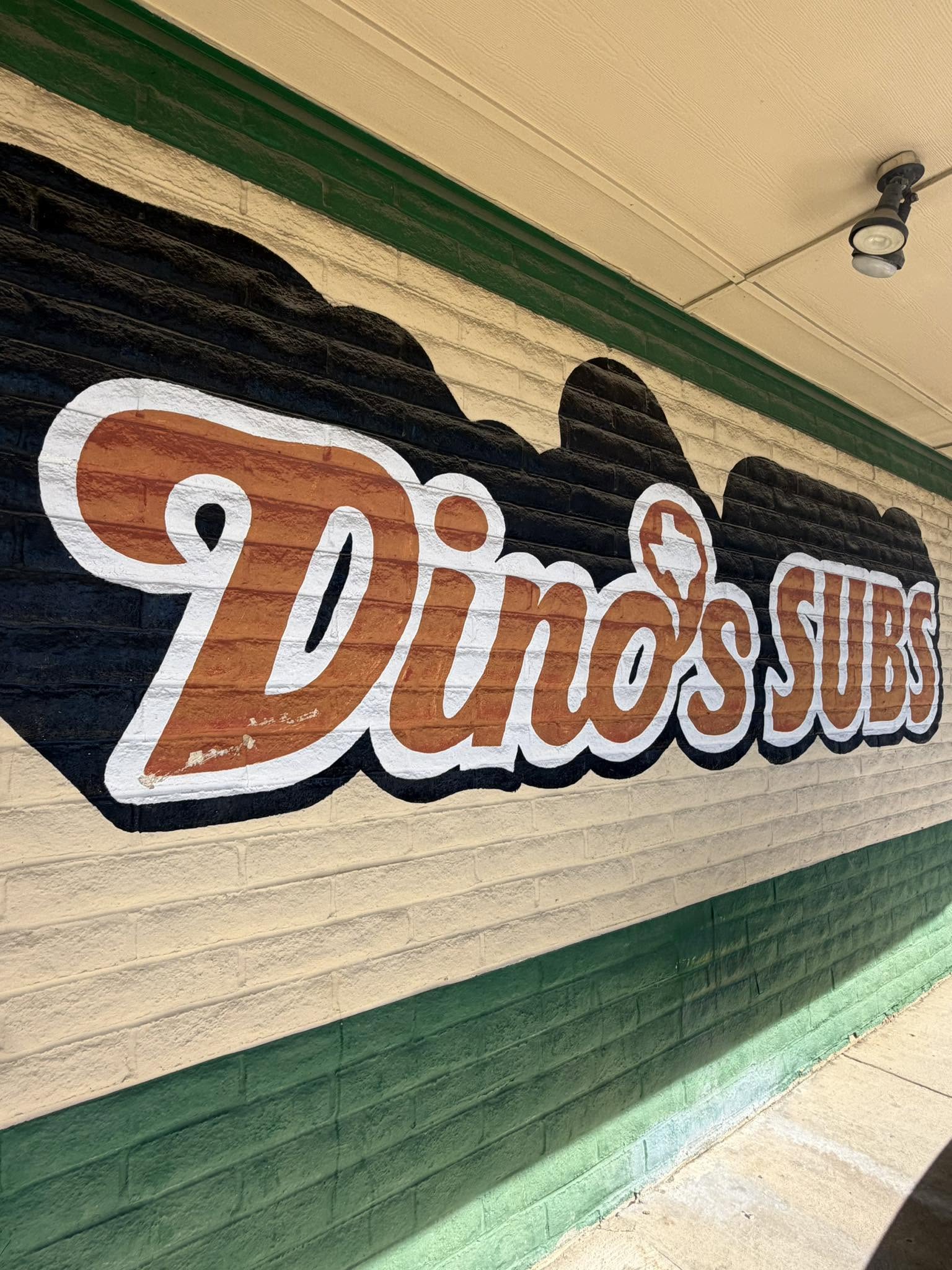 The painted Dino's Subs wordmark on the restaurant wall
